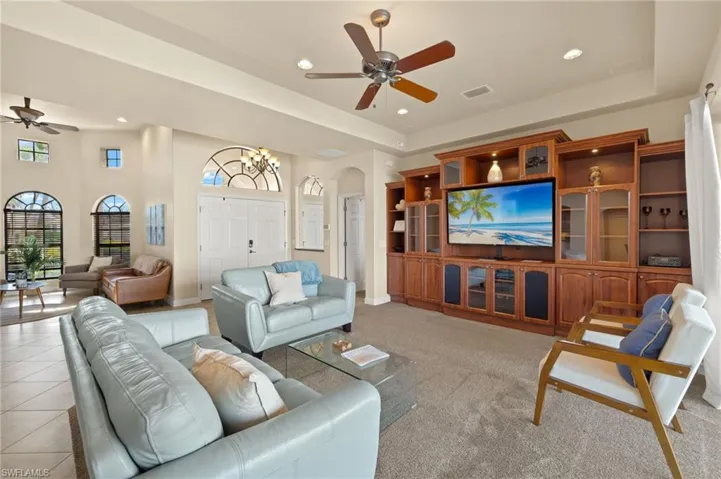 Living room featuring a ceiling fan, arched walkways, a tray ceiling, recessed lighting, and baseboards