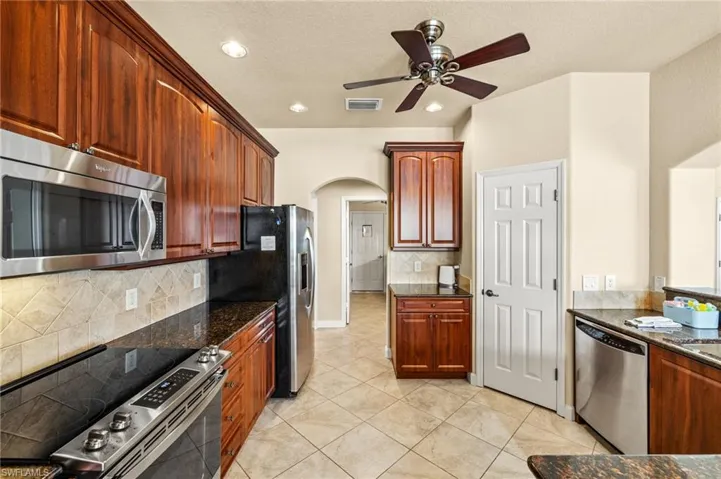 Kitchen featuring stainless steel appliances, arched walkways, a ceiling fan, dark stone counters, and decorative backsplash