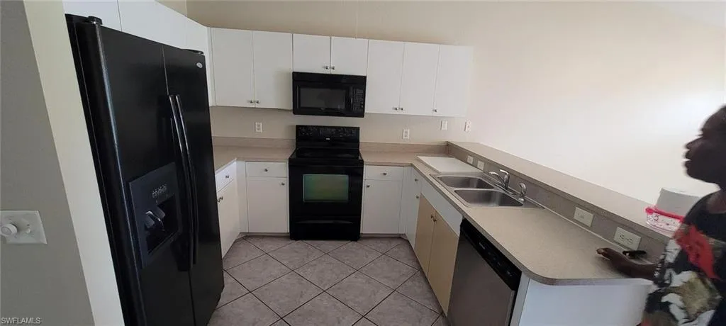 Kitchen with black appliances, light tile patterned floors, white cabinetry, and light countertops