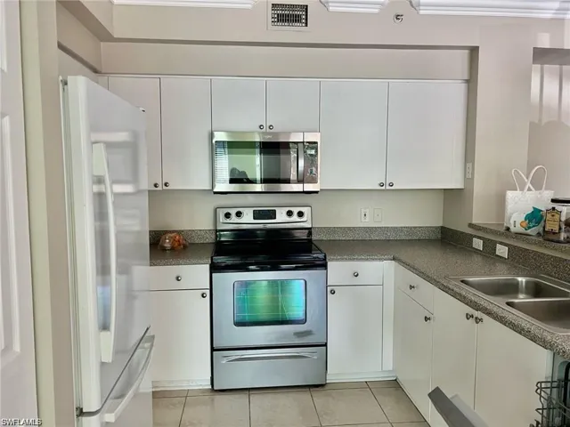 Kitchen featuring appliances with stainless steel finishes, white cabinetry, light tile patterned floors, and dark countertops