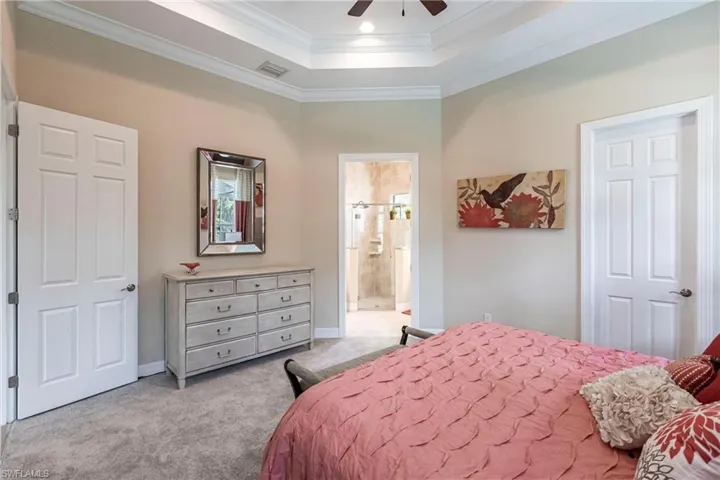 Bedroom featuring ensuite bathroom, light colored carpet, visible vents, ornamental molding, and a tray ceiling