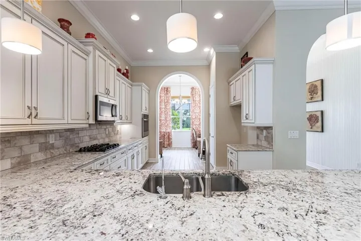 Kitchen featuring arched walkways, a sink, appliances with stainless steel finishes, light stone countertops, and pendant lighting