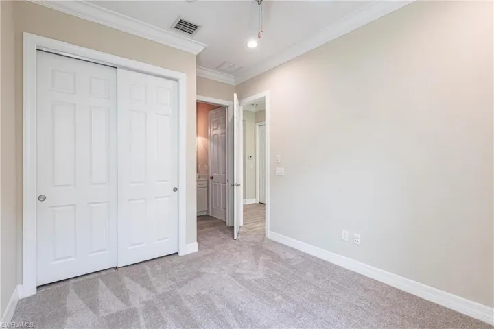 Unfurnished bedroom featuring baseboards, visible vents, light colored carpet, ornamental molding, and a closet