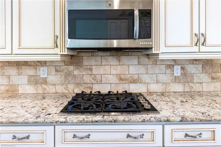 Kitchen featuring tasteful backsplash, stainless steel microwave, gas stovetop, and light stone countertops