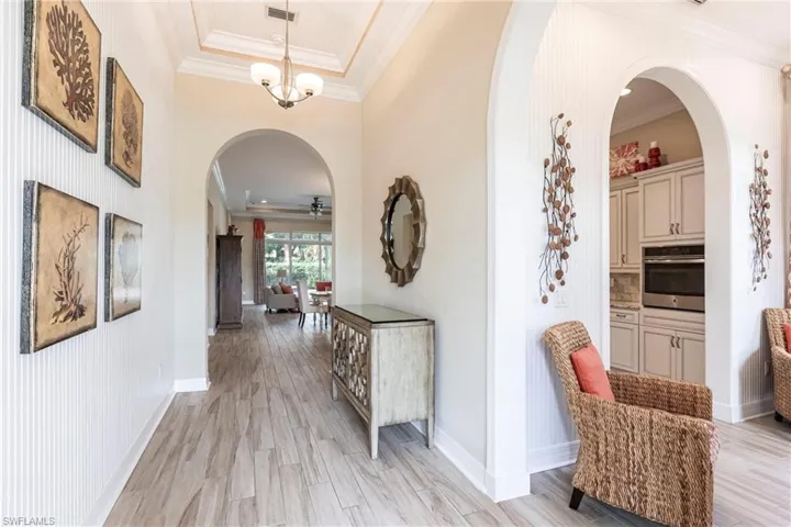 Hall featuring arched walkways, visible vents, crown molding, and light wood-style tile