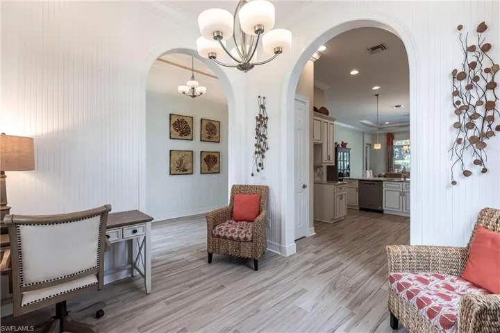 Sitting room with light wood-style floors, arched walkways, visible vents, and crown molding