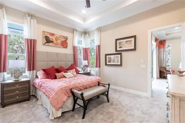 Bedroom with light carpet, baseboards, ornamental molding, and a raised ceiling with recess lighting and fan