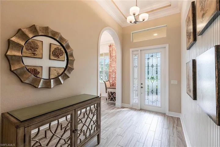 Entryway with arched walkways, baseboards, a tray ceiling, light wood finished tile floors, and crown molding