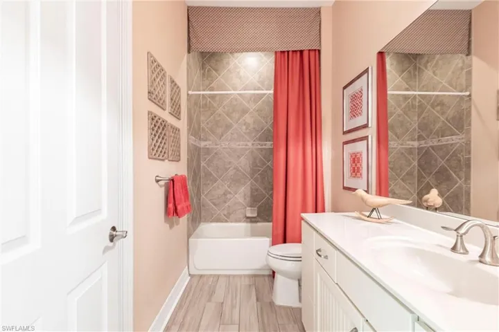Full bath featuring shower / bath combination with curtain, toilet, vanity, wood finished floors, and baseboards