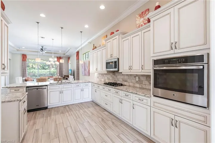 Kitchen featuring a peninsula, hanging light fixtures, appliances with stainless steel finishes, backsplash, and crown molding