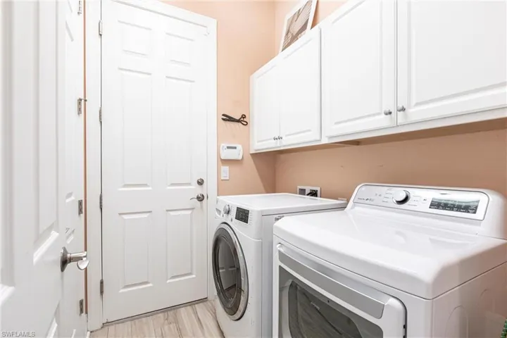 Clothes washing area with light wood-tile flooring, cabinet space, and washer and dryer