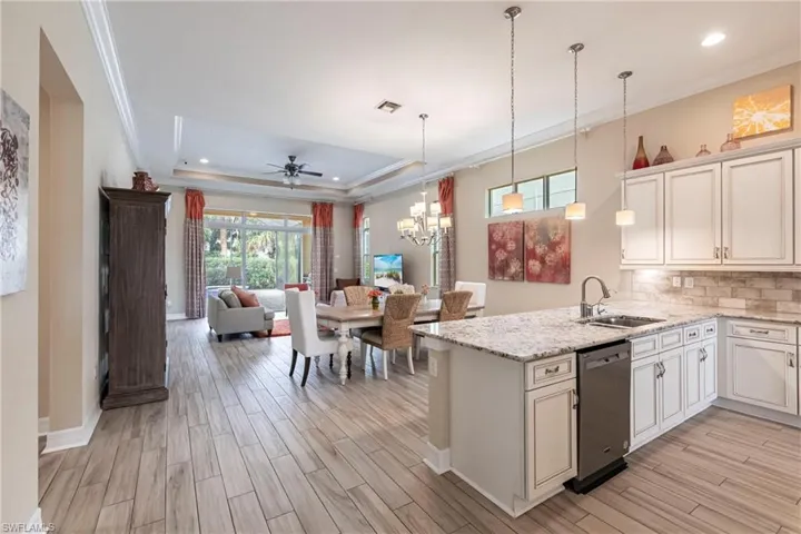 Kitchen featuring a sink, white cabinetry, open floor plan, dishwasher, and pendant lighting