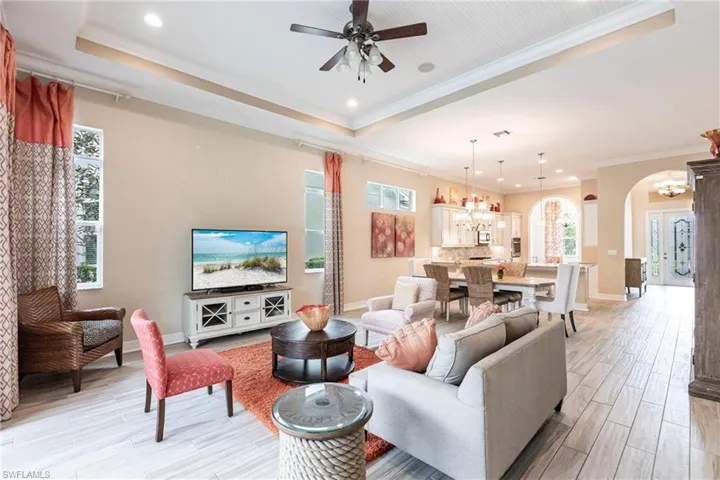 Living room with arched walkways, a tray ceiling, crown molding, light wood-style tile flooring, and baseboards