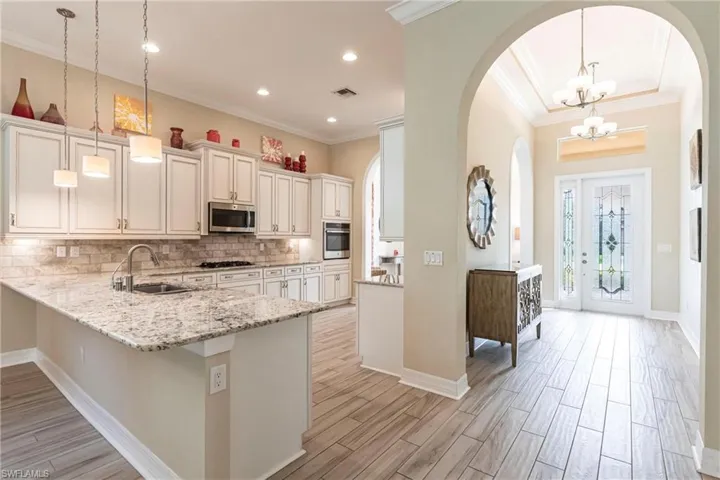 Kitchen with visible vents, hanging light fixtures, a peninsula, stainless steel appliances, and a sink and tile backsplash