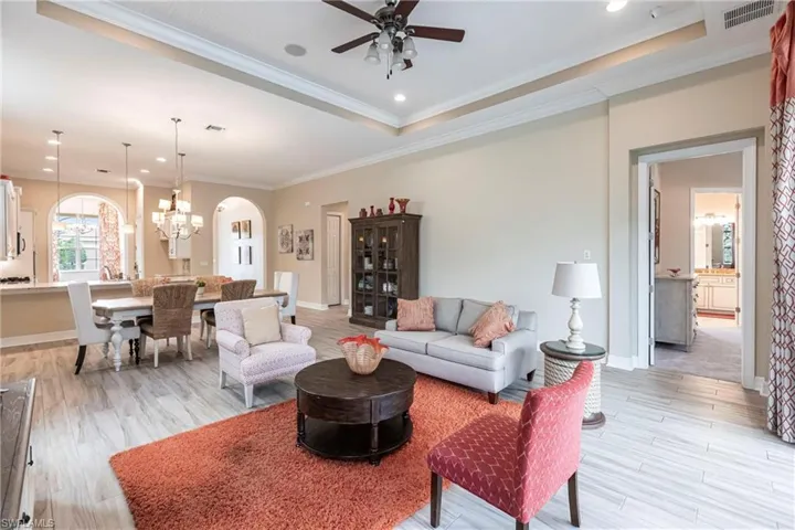 Living area featuring arched walkways, a tray ceiling, visible vents, ornamental molding, and light wood-style floors