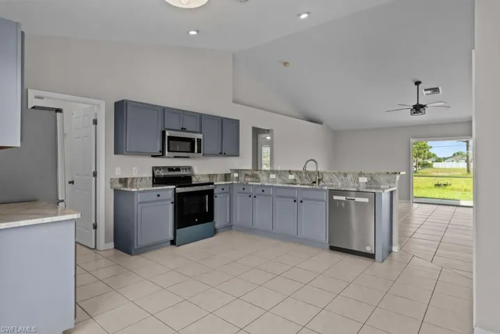 Kitchen featuring gray cabinetry, appliances with stainless steel finishes, light tile patterned floors, a peninsula, and high vaulted ceiling