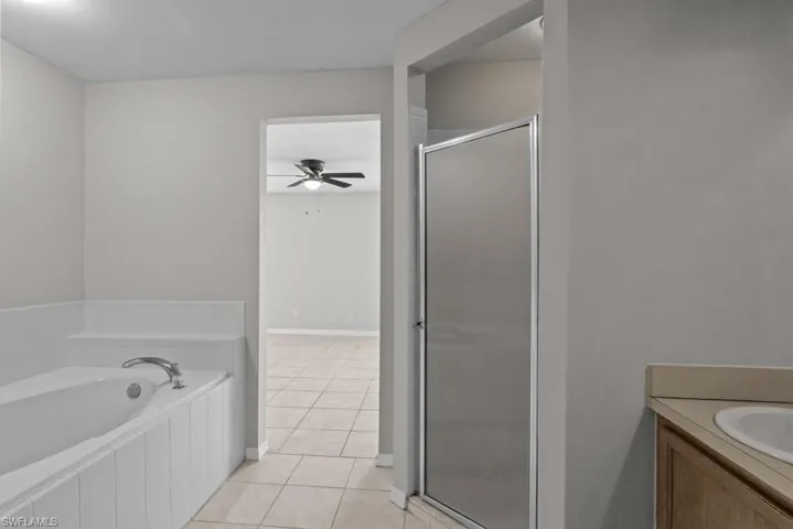 Full bath with vanity, light tile patterned flooring, a stall shower, a garden tub, and a ceiling fan