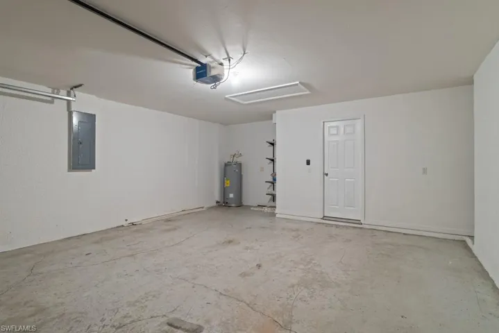 Garage featuring electric panel, electric water heater, and a garage door opener