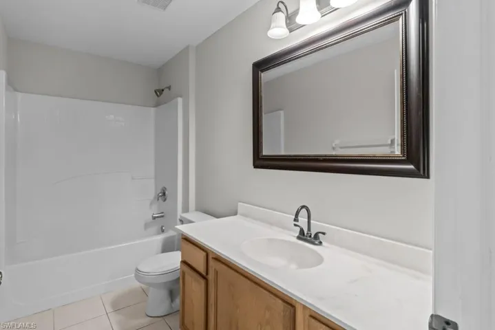 Bathroom featuring washtub / shower combination, light tile patterned floors, and vanity