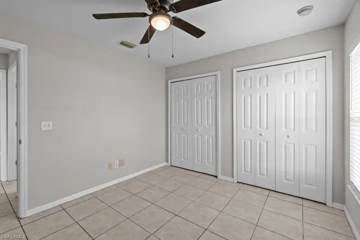 Unfurnished bedroom featuring light tile patterned floors, multiple closets, and a ceiling fan