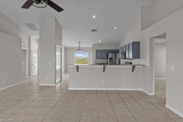 Kitchen with a kitchen bar, a peninsula, high vaulted ceiling, light tile patterned floors, and decorative light fixtures