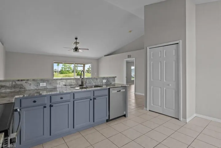 Kitchen with light stone countertops, stainless steel appliances, light tile patterned floors, gray cabinetry, and high vaulted ceiling
