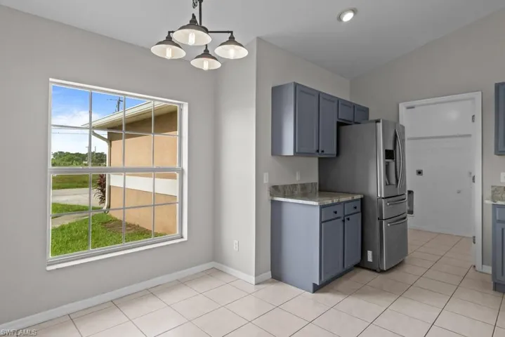 Kitchen featuring hanging light fixtures, light tile patterned floors, stainless steel fridge with ice dispenser, gray cabinetry, and a chandelier
