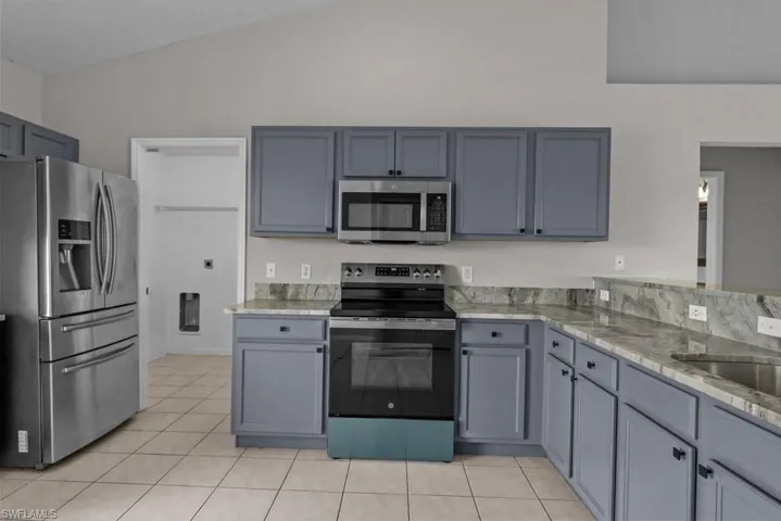 Kitchen featuring appliances with stainless steel finishes, gray cabinetry, light tile patterned flooring, light stone countertops, and high vaulted ceiling