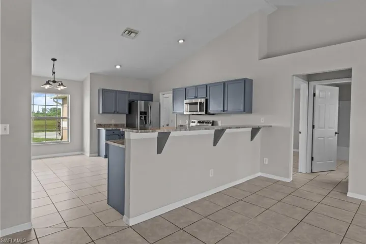 Kitchen with a breakfast bar, a peninsula, stainless steel appliances, high vaulted ceiling, and light tile patterned flooring
