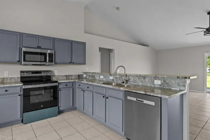 Kitchen featuring appliances with stainless steel finishes, a peninsula, gray cabinets, light tile patterned flooring, and ceiling fan