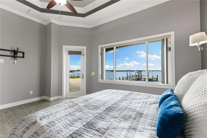 Bedroom featuring ornamental molding, a tray ceiling, a water view, hardwood / wood-style floors, and ceiling fan