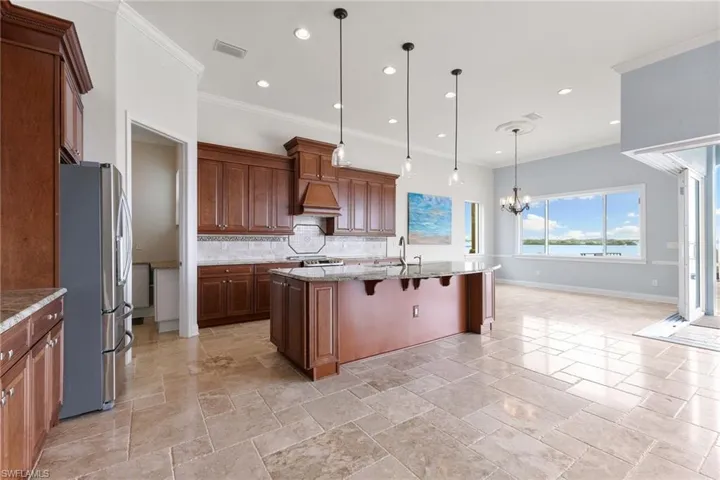 Kitchen with an island with sink, stainless steel refrigerator, pendant lighting, tasteful backsplash, and custom exhaust hood