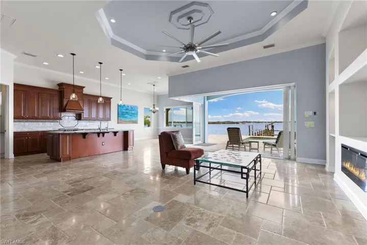 Living room with ceiling fan, a tray ceiling, crown molding, sink, and light tile floors