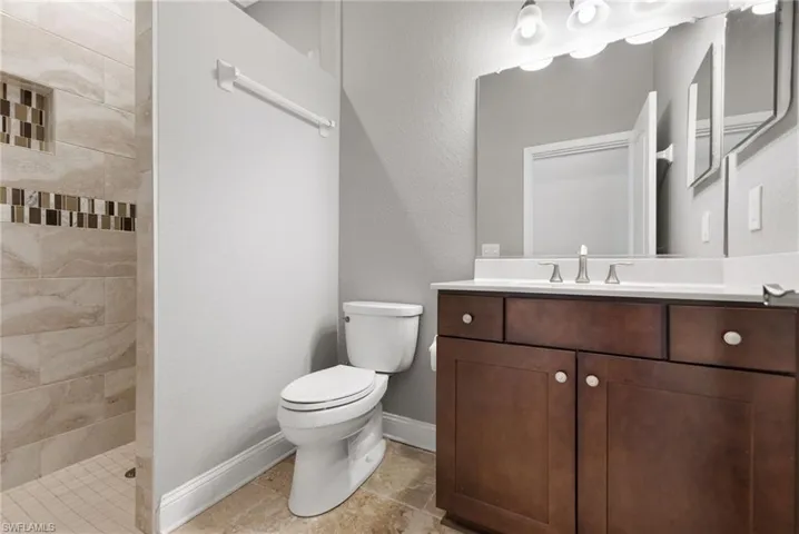 Bathroom featuring a tile shower, tile flooring, toilet, and vanity