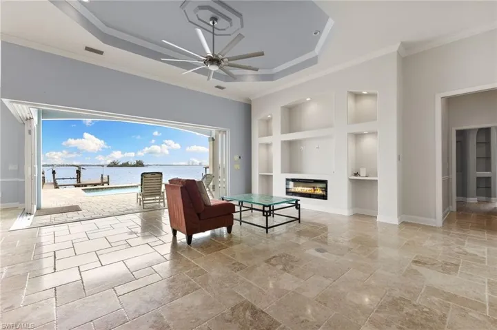 Living area with light tile floors, built in shelves, and a raised ceiling