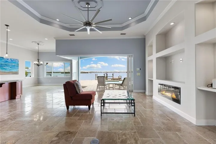 Tiled living room featuring a tray ceiling, ornamental molding, built in features, and ceiling fan with notable chandelier