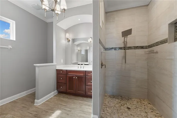 Bathroom with oversized vanity, wood-type flooring, an inviting chandelier, a tile shower, and ornamental molding