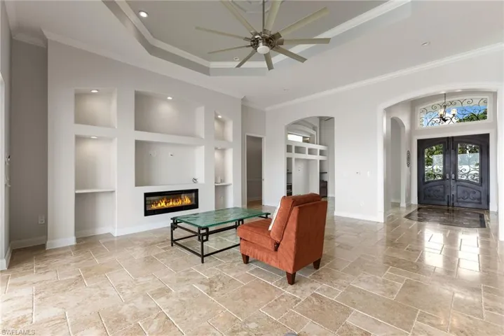 Tiled living room featuring ceiling fan, built in shelves, crown molding, and french doors