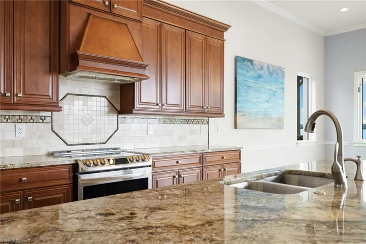 Kitchen with stainless steel stove, premium range hood, light stone counters, sink, and tasteful backsplash