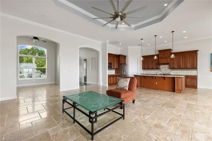 Living room featuring light tile flooring, ceiling fan, a tray ceiling, and crown molding