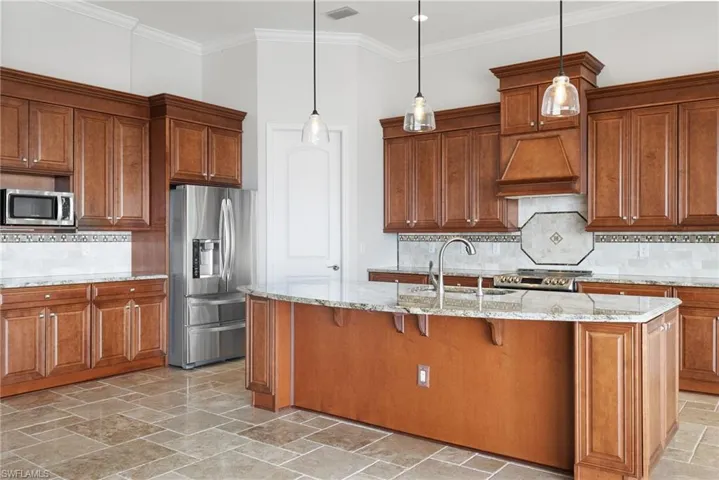 Kitchen featuring appliances with stainless steel finishes, an island with sink, backsplash, pendant lighting, and custom exhaust hood