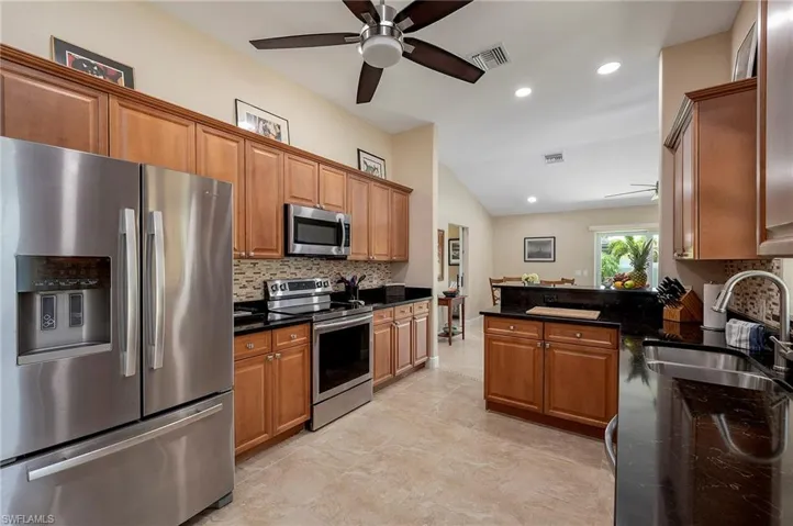 Kitchen with tasteful backsplash, ceiling fan, dark stone countertops, appliances with stainless steel finishes, and light tile patterned floors