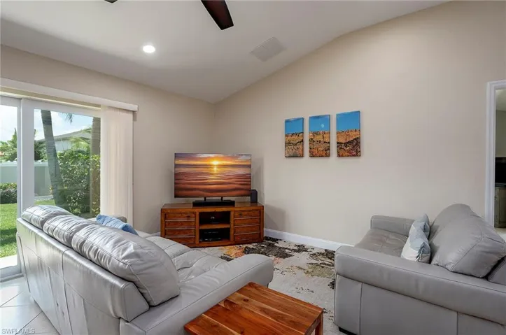 Living room with light tile patterned floors, a wealth of natural light, lofted ceiling, and ceiling fan