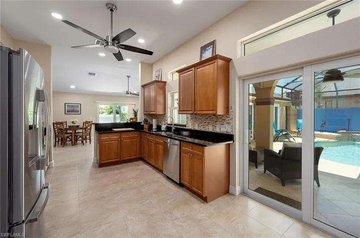 Kitchen with appliances with stainless steel finishes, kitchen peninsula, backsplash, light tile patterned floors, and ceiling fan