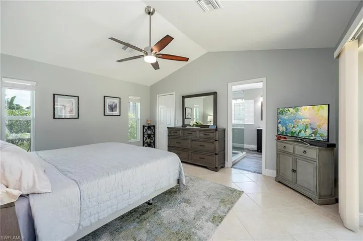 Bedroom featuring lofted ceiling, light tile patterned floors, connected bathroom, ceiling fan, and a closet