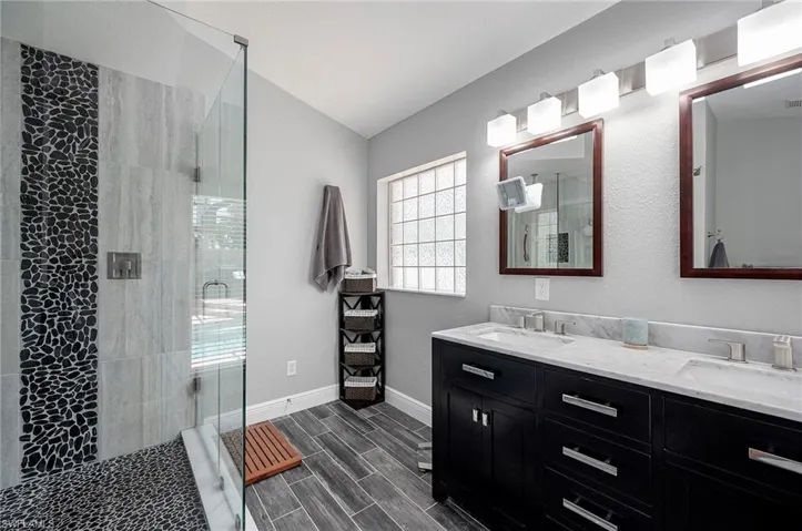 Bathroom featuring double vanity, walk in shower, and vaulted ceiling