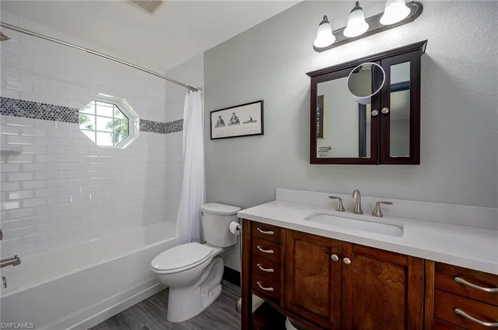 Full bathroom featuring shower / bath combo with shower curtain, vanity, hardwood / wood-style flooring, and toilet