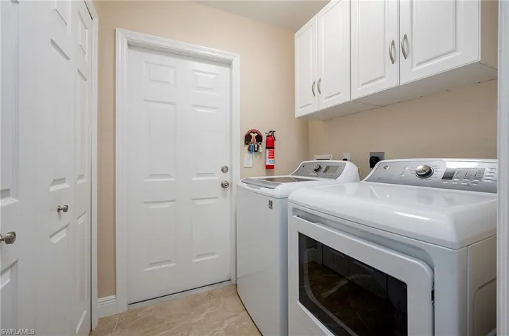 Clothes washing area with washer and dryer, cabinets, and light tile patterned floors