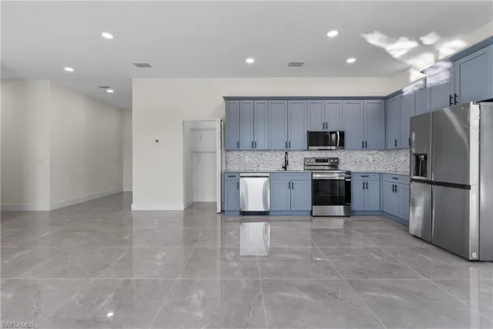 Kitchen with appliances with stainless steel finishes, recessed lighting, light marble finish flooring, tasteful backsplash, and open floor plan