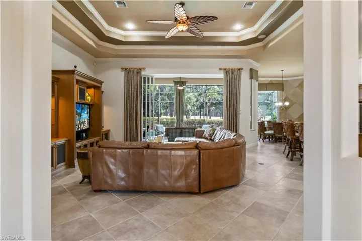 Tiled living room with a raised ceiling, ornamental molding, and ceiling fan